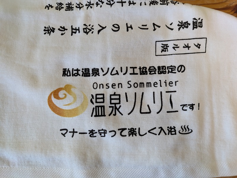 温泉ソムリエ認定タオルのアップ。「私は温泉ソムリエ協会認定の温泉ソムリエです！マナーを守って楽しく入浴」と書かれている